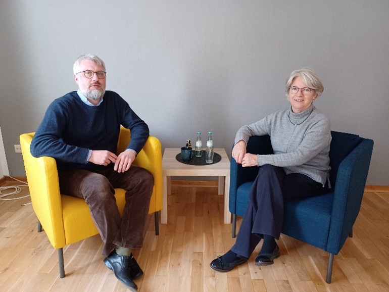 Thomas Taxacher und Johanna Pfeifer sitzen auf zwei Sesseln mit einem kleinen Tisch in der Mitte.