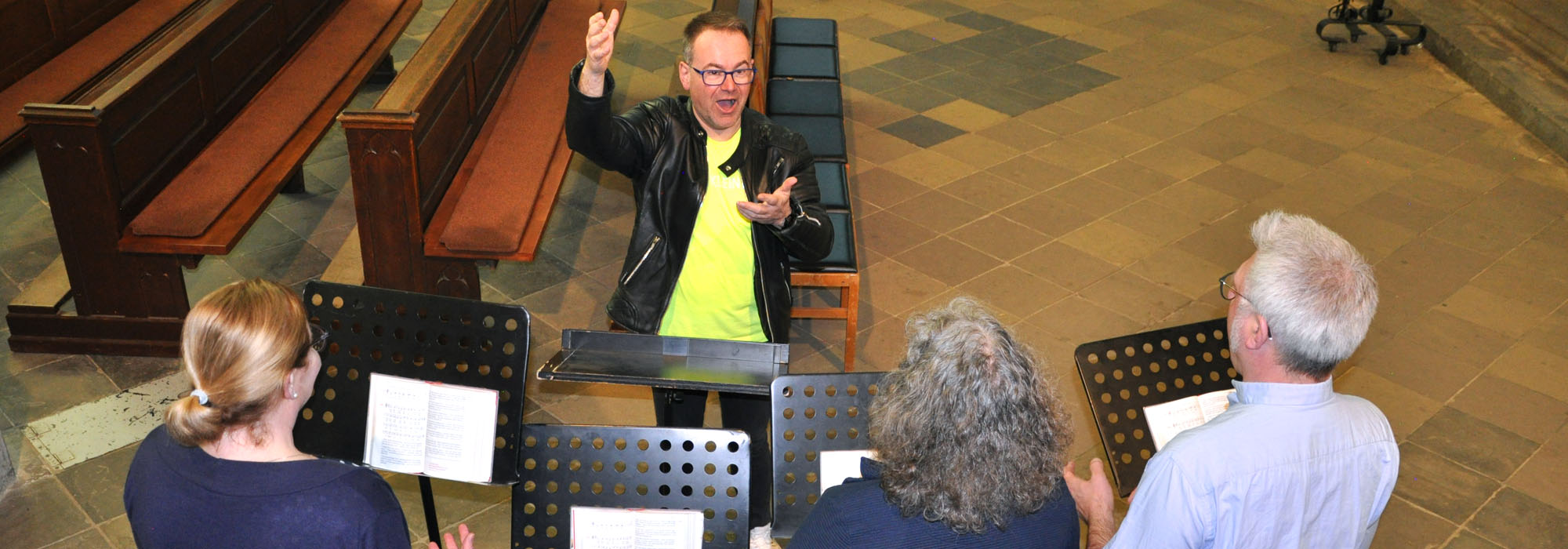 3 Chorsänger vor Chorleiter, ein leerer Platz