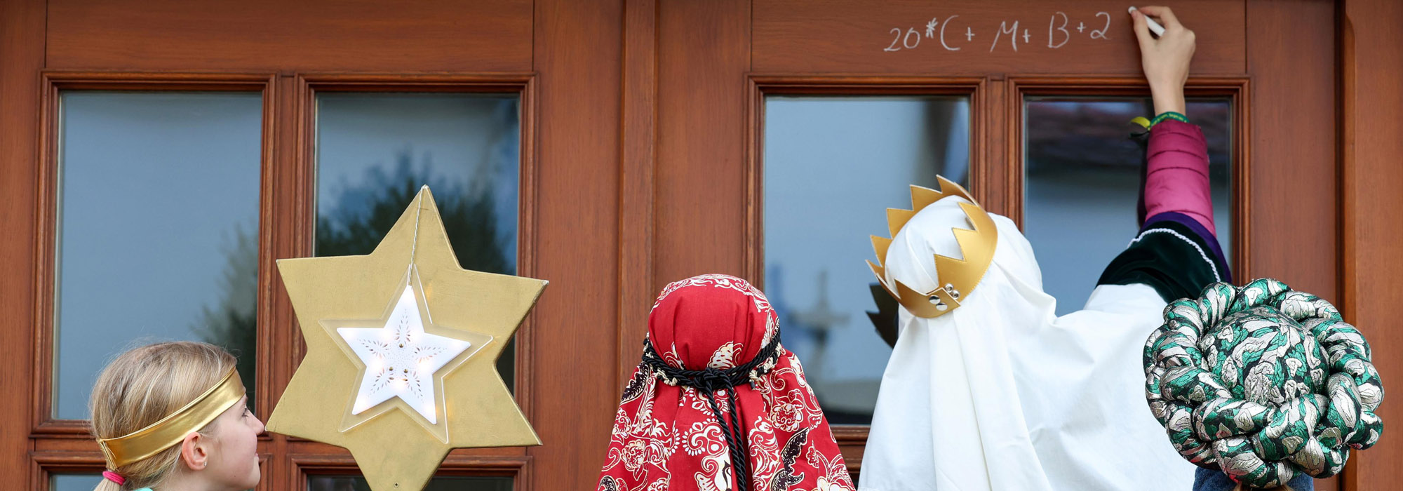 Sternsinger schreiben Segen über eine Haustür